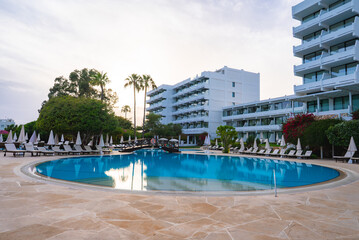 A large circular pool with lounge chairs, umbrellas, and a decorative bridge, surrounded by palm...