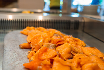 Thinly sliced smoked salmon displayed on a stone or metal surface indoors, with vibrant orange tones and a blurred dining area in the background.