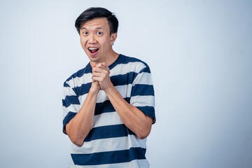 Asian man in striped shirt clapping his hands with a playful and cheerful expression, standing...