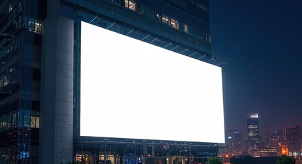 Illuminated blank billboard on modern building exterior at night in the city