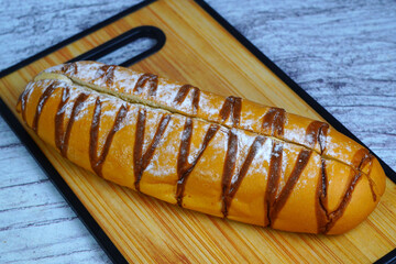 A golden-brown mocha loaf with chocolate drizzle and powdered sugar, resting on a wooden cutting...