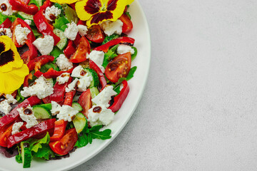 Fresh vegan salad with tomatoes, arugula, goat cheese, olives, and edible flowers on a white plate