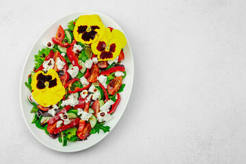 Fresh vegan salad with tomatoes, arugula, goat cheese, olives, and edible flowers on a white plate