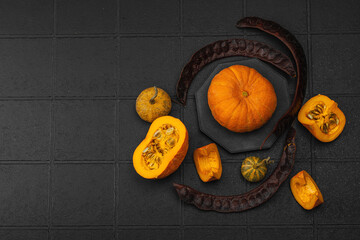 Organic ornamental pumpkins with textured skin and cut slices on dark background. Natural concept