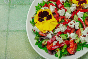 Fresh vegan salad with tomatoes, arugula, goat cheese, olives, and edible flowers on a white plate