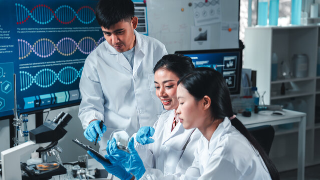 Young researchers collaborate in a high-tech lab, smiling and discussing data on a digital tablet. Surrounded by lab tools and digital screens, they represent teamwork, diversity, and innovation.
