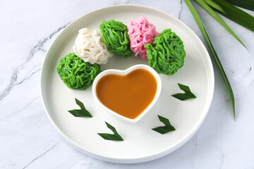 Kue Putu Mayang, a traditional Indonesian steamed cake, features unique noodle-like strands made from rice flour. It's served on a white plate with liquid palm sugar sauce (kinca). 