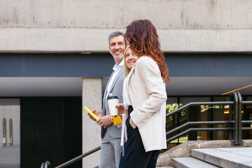 Businesspeople discussing contract outdoors while holding coffee and tablet