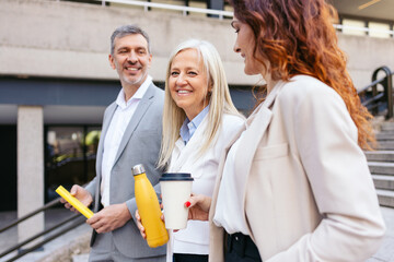 Business people walking outside office building, holding reusable coffee cup and water bottle, discussing work