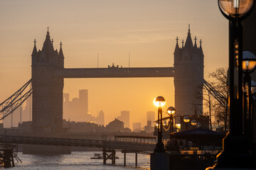 Sunrise casts a warm glow on Tower Bridge as it stands majestically over the River Thames. The surrounding city skyline fades into the background, creating a stunning silhouette.