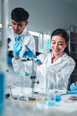 A female scientist in a white lab coat and blue gloves closely examines a petri dish with visible...