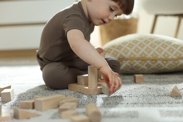 Cute little child playing with wooden building blocks at home, closeup