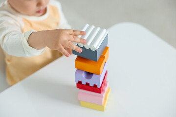 Cute little child playing with building bricks at white table indoors, closeup