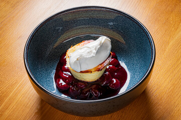 Luxurious dessert showcases a golden pastry topped with fluffy cream, served on sweet cherries