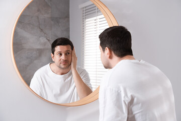 Handsome man looking at himself in mirror indoors