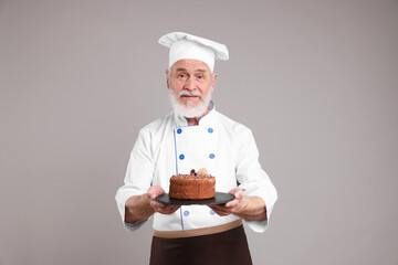 Professional pastry chef with delicious chocolate cake on grey background