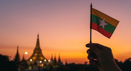 Hand proudly displaying Myanmar flag against a serene sunset cityscape backdrop
