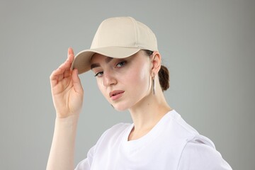 Beautiful woman in stylish baseball hat on grey background, closeup