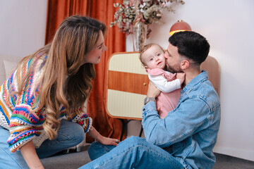 Touching family moment with father holding and kissing his baby girl as mother looks on. Captured...