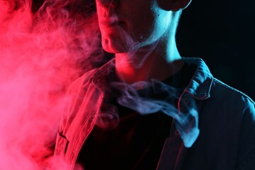 Man using electronic smoking device in neon lights on black background, closeup