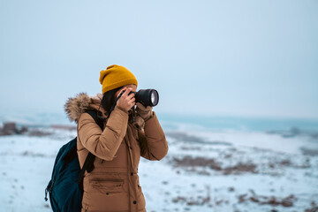 Young womanphotographer taking photo with professional camera in a winter day.