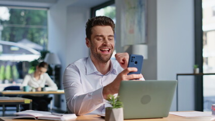 Company worker watching funny video on cellphone sitting office desk closeup.