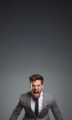  Homme en costume gris hurlant de colère, expression faciale intense et posture tendue sur fond gris uni espace négatif copyspace