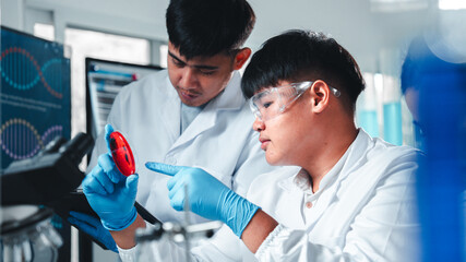 A diverse group of young scientists collaborate in a modern lab, examining a petri dish with bacterial cultures while taking notes, emphasizing teamwork, research, and scientific discovery.