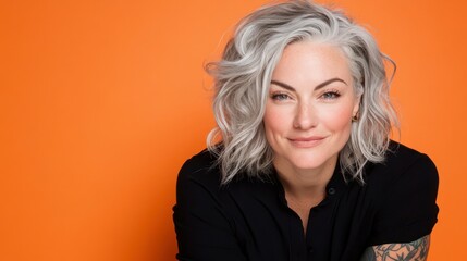 Naklejka premium Smiling Beauty in Simplicity: A portrait showcases a woman with striking silver hair and a warm smile, her gaze engaging. Against a vibrant orange background.