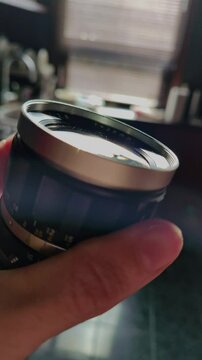 A close-up shot captures an artistic and technical mood as a hand holds a vintage camera lens, featuring its aperture and focus rings, with a prominent lens flare suggesting creative photography