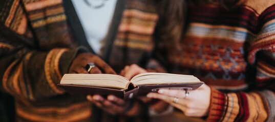 Two individuals sharing a book in a cozy setting wearing warm patterned sweaters