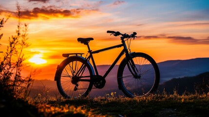Fototapeta premium Silhouette of a bicycle at sunrise, placed on a hilltop overlooking a valley, with warm colors of dawn lighting the sky.