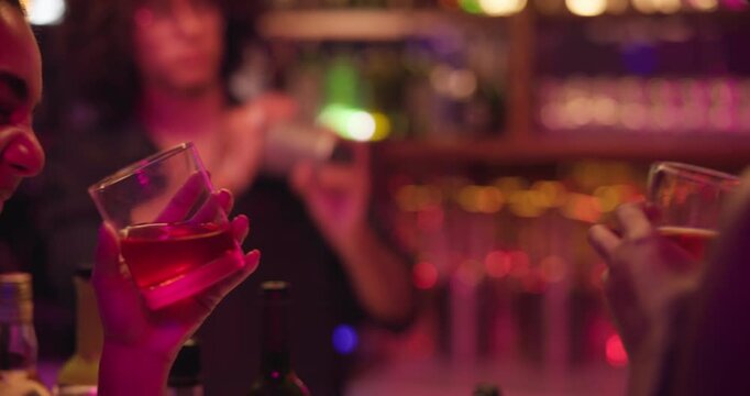 Friends, drink and toast with people at a pub for celebration, fun or night out at bartender counter. Women, cheers and alcohol glass at bar or nightclub for drinking, social event and party