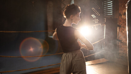 A female boxer with short hair and a black T-shirt. athletic appearance, pause after an intense workout, Leaning on a punching bag, The cinematic look and mood of a motivational story