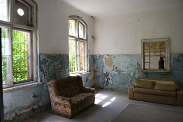 altes Sofa in Abbruchhaus in Zimmer mit abblätternder Farbe und Fenster mit Blick ins Grüne