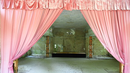 vergilbter ausgeblichener, roter Bühnenvorhang in Theaterbühne in Bauruine eines Theaters 