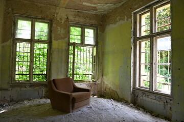 altes Sofa in Abbruchhaus in Zimmer mit abblätternder Farbe und Fenster mit Blick ins Grüne