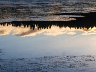 Tranquil winter scene in Sweden showcasing reflection of trees and clouds on icy water