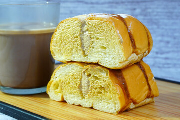 Close-up of sliced golden bread with chocolate drizzle and powdered sugar, filled with mocha cream, next to a mug of milk.