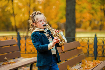 Little girl playing saxophone in autumn park on sunny day. Happy child practice music instrument...