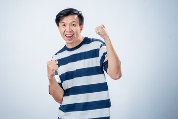 Asian man in striped shirt celebrating with clenched fists and joyful expression, showing excitement and triumph against a plain studio background