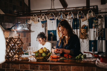 A warm scene of two friends preparing food together in a homey kitchen setting. The space is adorned with hanging mugs and colorful fruits, evoking a sense of comfort, friendship, and culinary joy.