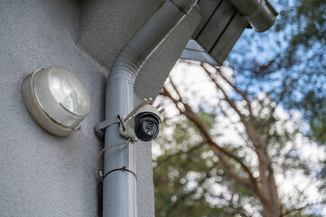 Security video camera mounted on corner of private house, close-up from below. Pine trees visible in background