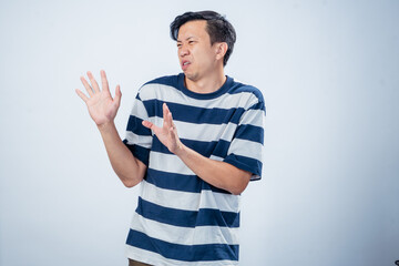 Asian man in navy and white striped t-shirt reacting with disgust and avoidance, raising both hands...