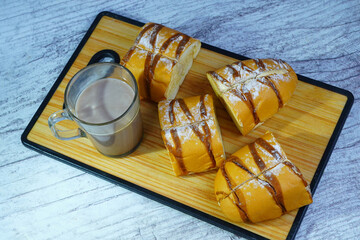A sliced mocha golden loaf with chocolate drizzle and powdered sugar, served with a glass of hot chocolate on a wooden board.