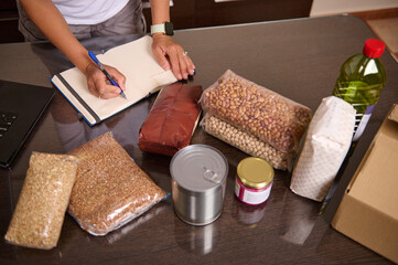Person Organizing Groceries Including Staple Items and Writing Notes on a Notebook