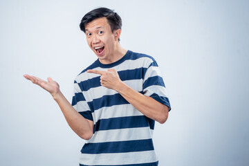 Asian man in striped shirt smiling and pointing excitedly to his open palm, posing against a plain...