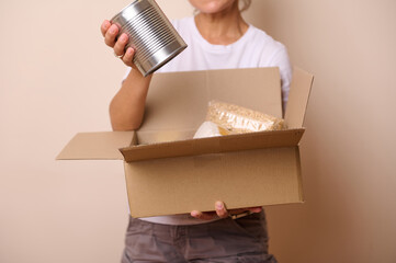Close-up hand of a volunteer woman packing goods into mockup cardboard box, preparing humanitarian...