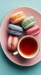 Obraz premium A top view of colorful macarons on a pink plate with a cup of tea on a light blue background