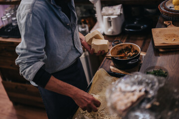 A person is seen adding cheese to a sheet, preparing a dish in a rustic kitchen.